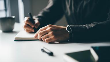 A man's hands close up writing in a notebook 