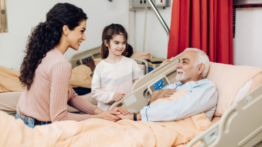 Man laying in hospital bed with a woman and female child by his bed side. 