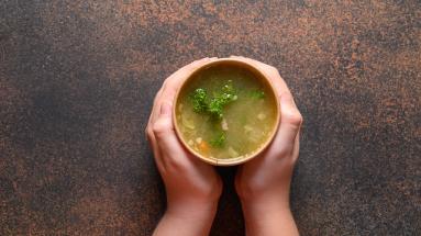 hands holding a cup of soup on both sides 