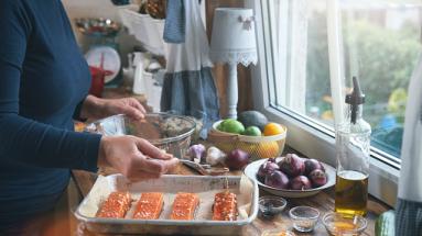 A woman prepping 4 pieces of salmon with a glaze on top