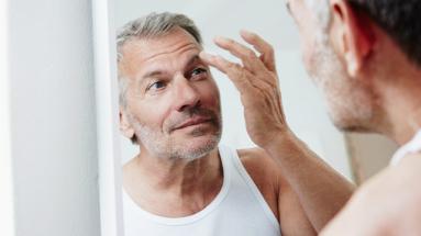 Man touching his eyebrow while looking in mirror