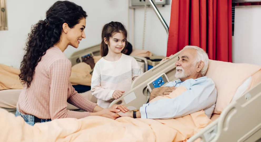 Man laying in hospital bed with a woman and female child by his bed side.