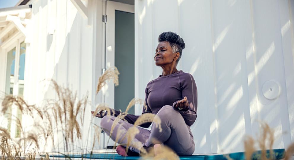 woman sitting outside criss cross apple sauce on yoga mat meditating