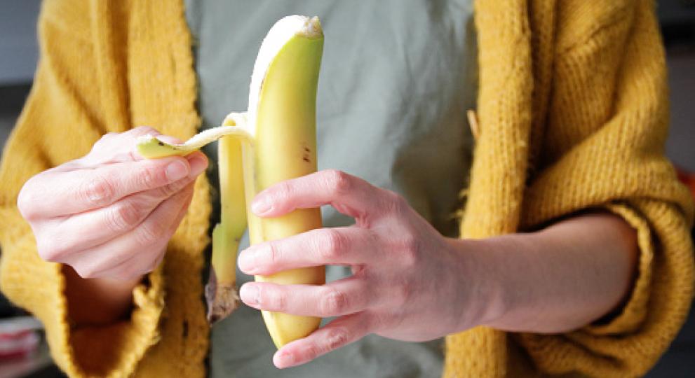 person in yellow sweater peeling a banana