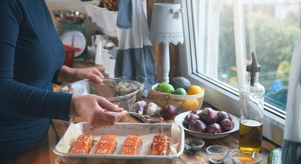 A woman prepping 4 pieces of salmon with a glaze on top