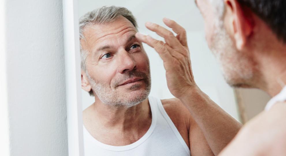 Man touching his eyebrow while looking in mirror